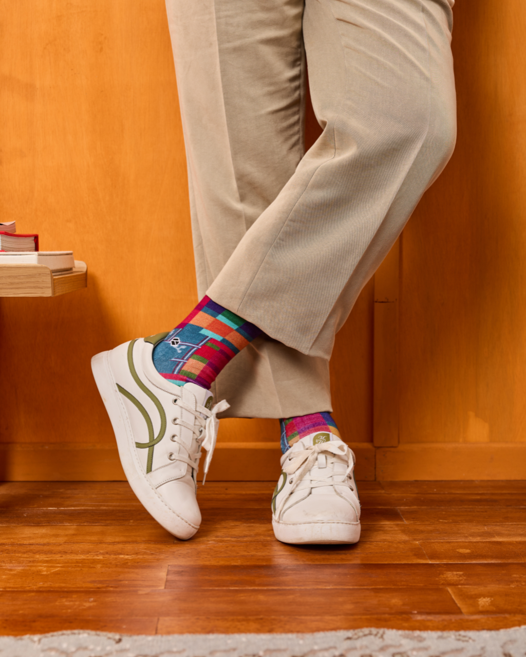 Person wearing colorful socks with white sneakers on a wooden floor.